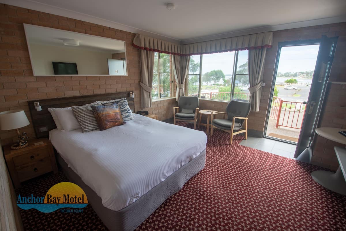 Quarto de hotel com uma cama grande, uma mesa, uma cadeira e uma varanda com vista.