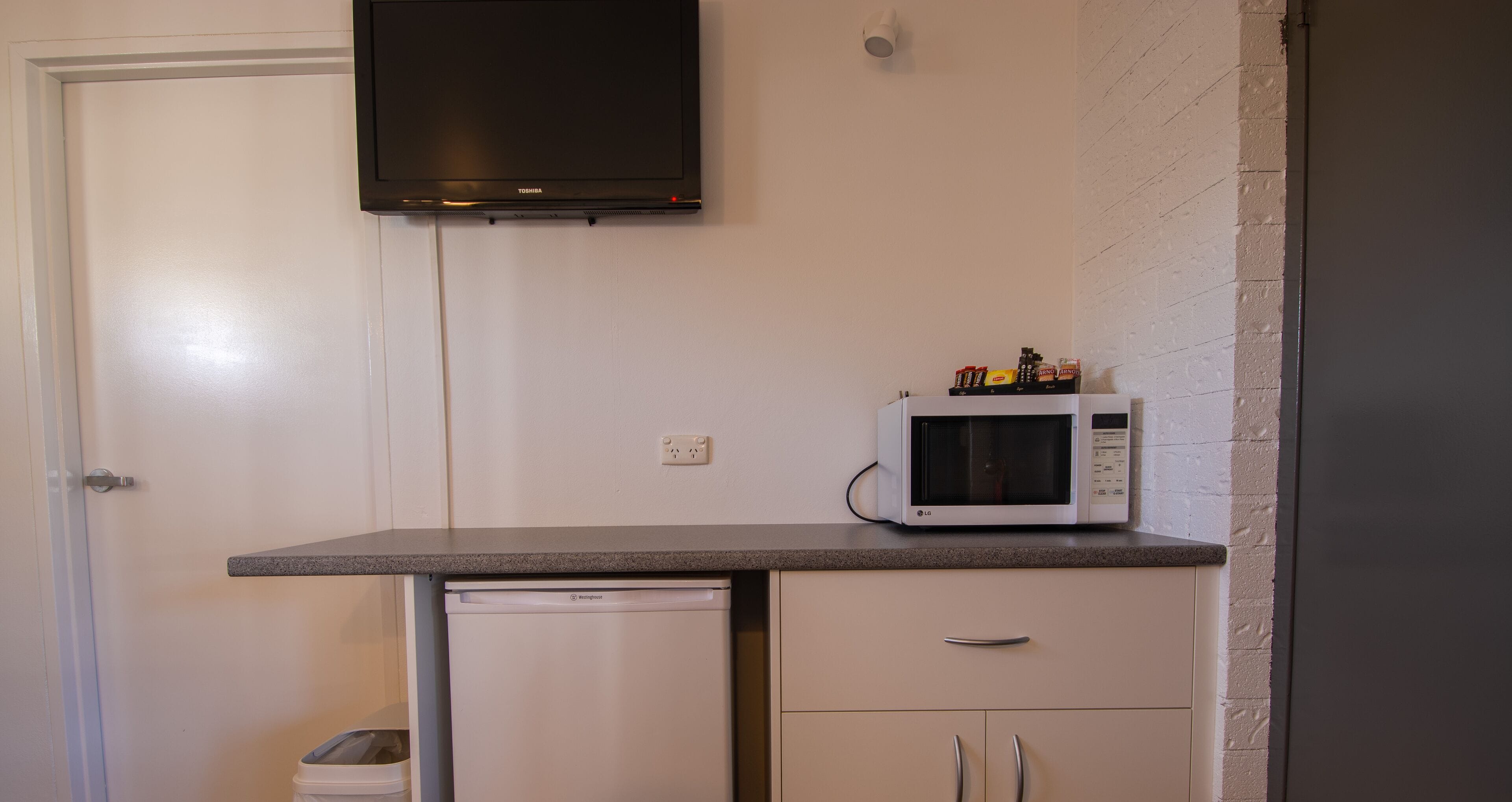 A compact kitchen with a microwave on the countertop, a small refrigerator, and a white door.