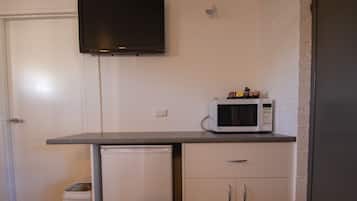 Una cocina compacta con microondas en la encimera, un refrigerador pequeño y una puerta blanca.