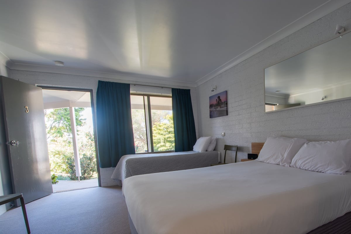 Quarto de hotel com duas camas, um espelho grande e vista para o verde lá fora.