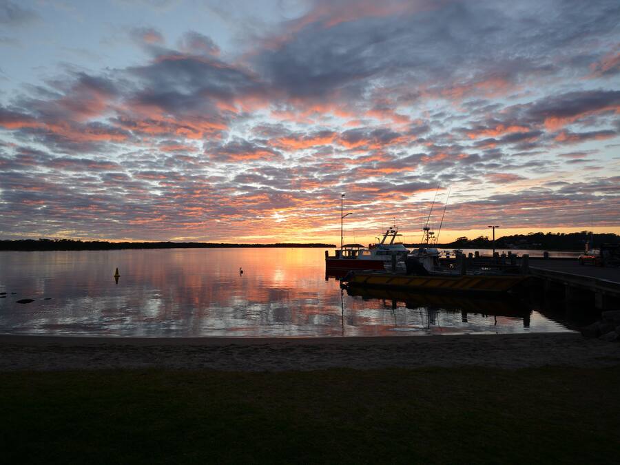 Un coucher de soleil sur un lac paisible, avec un quai et des bateaux.