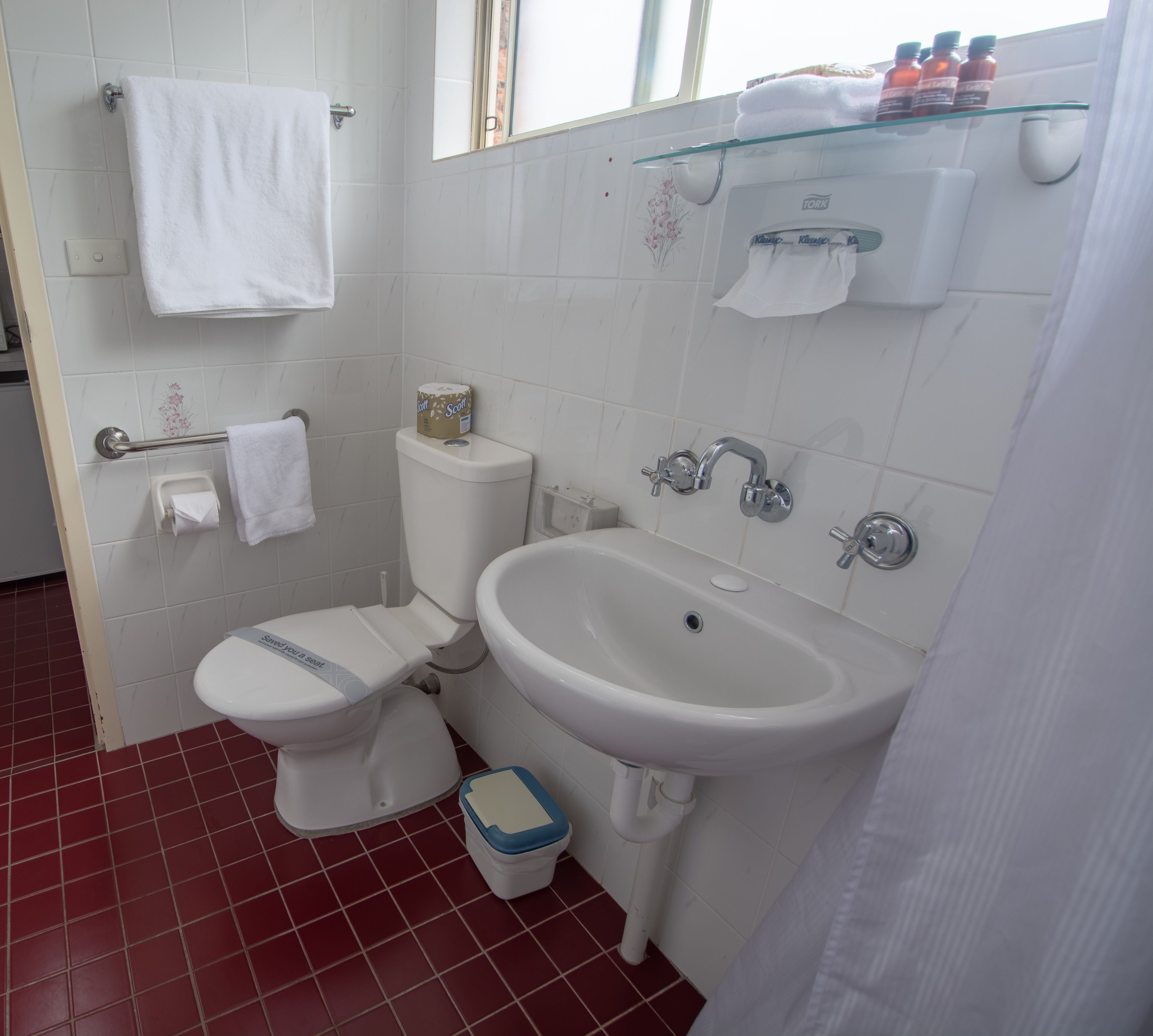 A bathroom with a toilet, sink, and a glass shelf with toiletries.