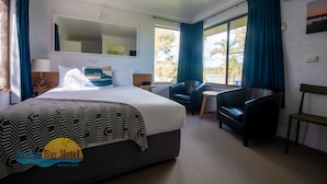 Habitación de hotel con una cama grande, un escritorio, una silla y un ventanal con cortinas.