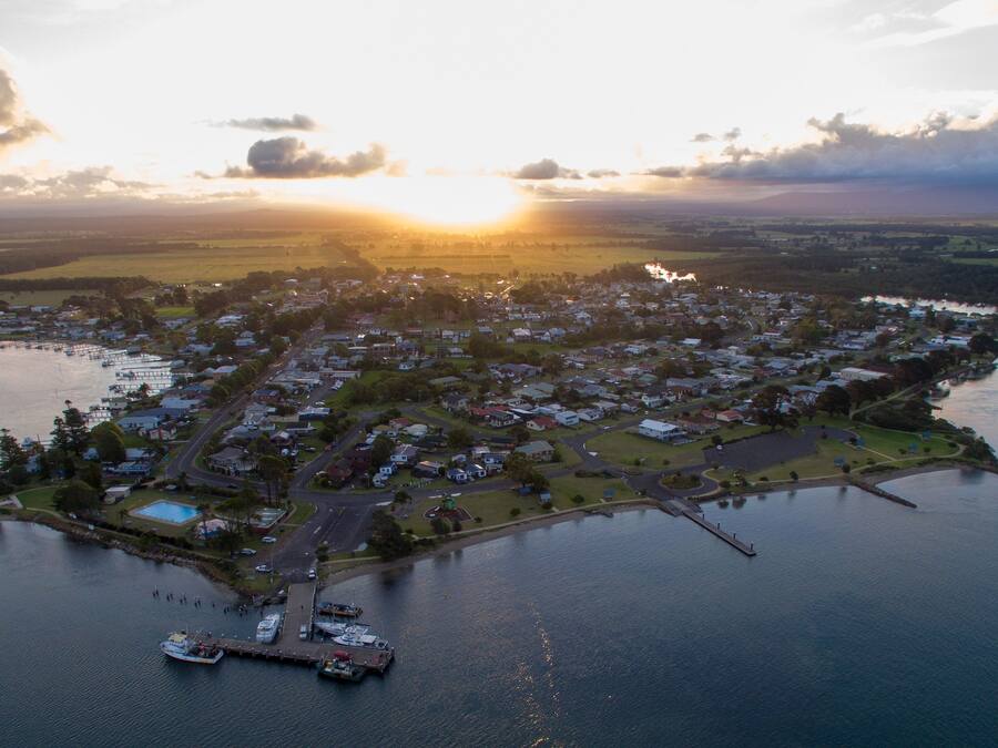 Vista aérea de un pueblo costero con un puerto deportivo, zonas residenciales y una gran extensión de agua.