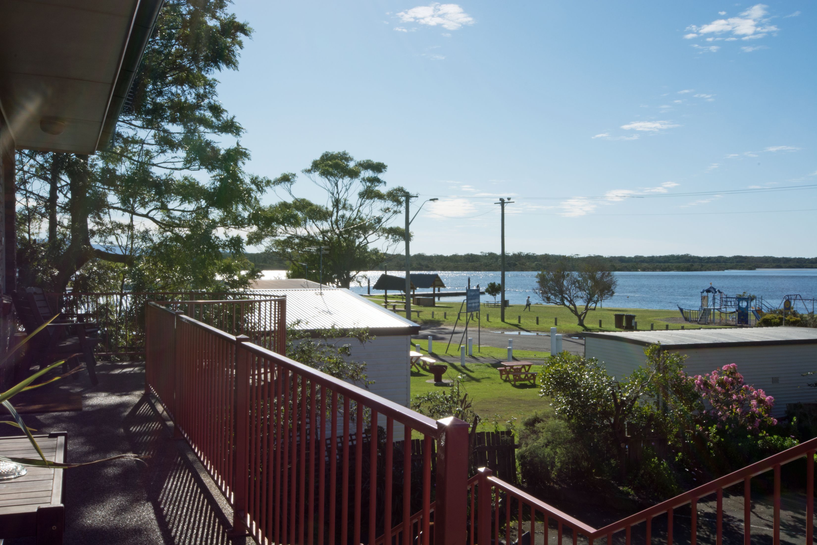 Uma varanda com vista para um lago, um parquinho e um edifício com telhado branco.