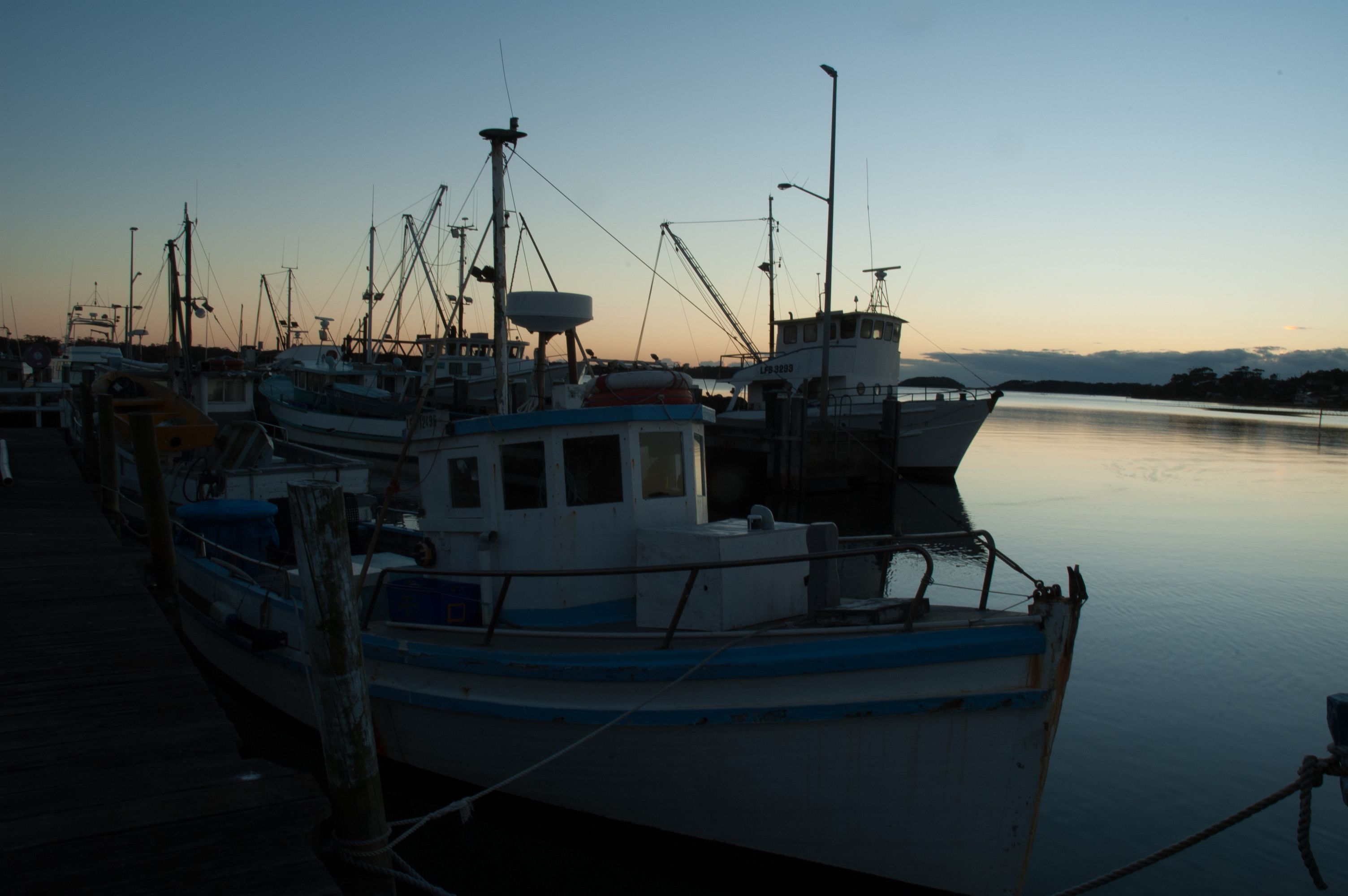 Un port de plaisance où plusieurs bateaux sont amarrés, l’eau est calme et le ciel est dégagé.