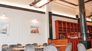 A restaurant with wooden tables and chairs, a bar area with shelves of bottles, and two framed pictures on the wall. - Alpha Hotel (Ostend)