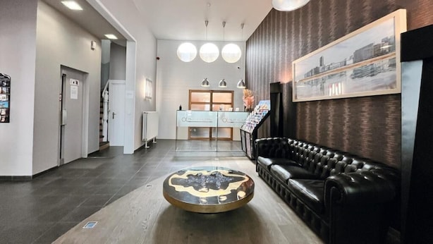 A modern lobby with a round coffee table, a black leather sofa, and a reception desk. - Alpha Hotel (Ostend)