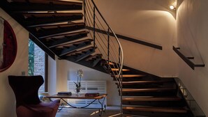 Un interior moderno con una escalera espiral, una silla roja, una mesa con libros y un jarrón con flores.