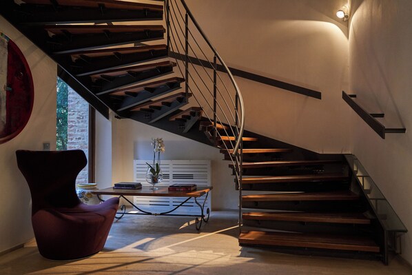 A modern interior with a spiral staircase, a red chair, a table with books, and a vase with flowers. - Poggio Piglia (Chiusi)