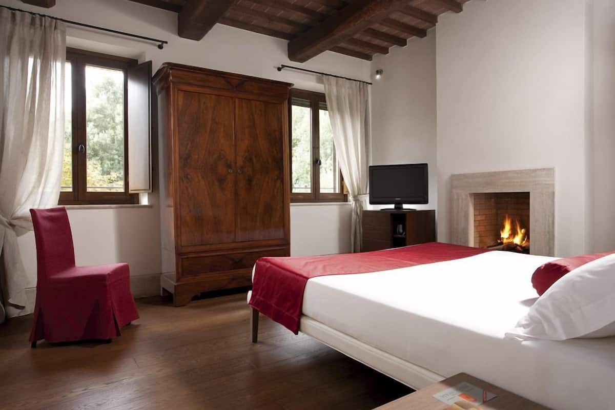 A bedroom with a bed, a wooden wardrobe, a TV, and a fireplace.