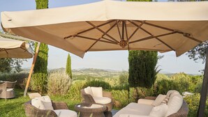 Zona de estar exterior con mobiliario de mimbre y sombrillas beige, con vistas a un paisaje pintoresco.