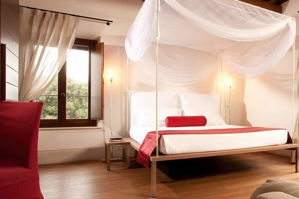 A bedroom with a canopy bed, wooden flooring, and a red chair.