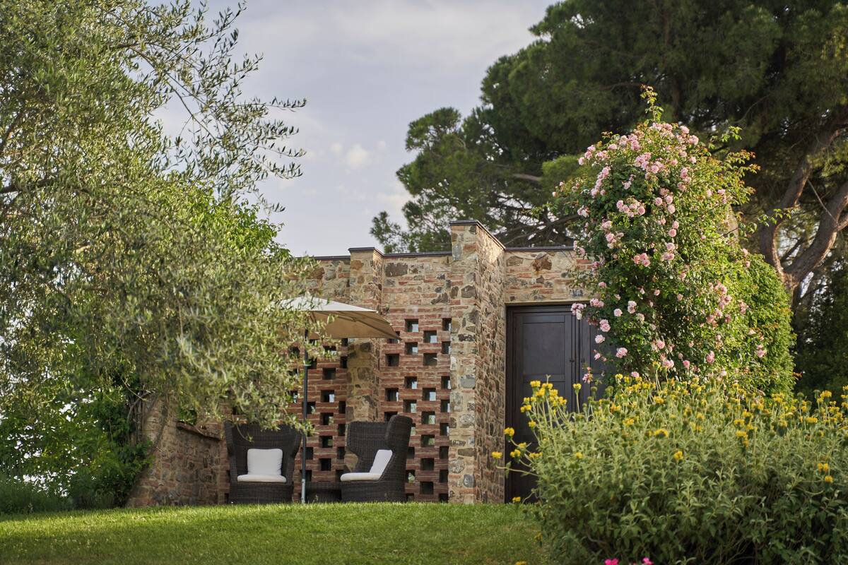 A stone building with a brick wall, a door, and two white lounge chairs under an umbrella.