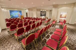 Un salón de conferencias con filas de sillas rojas y una pantalla grande mostrando un gráfico.