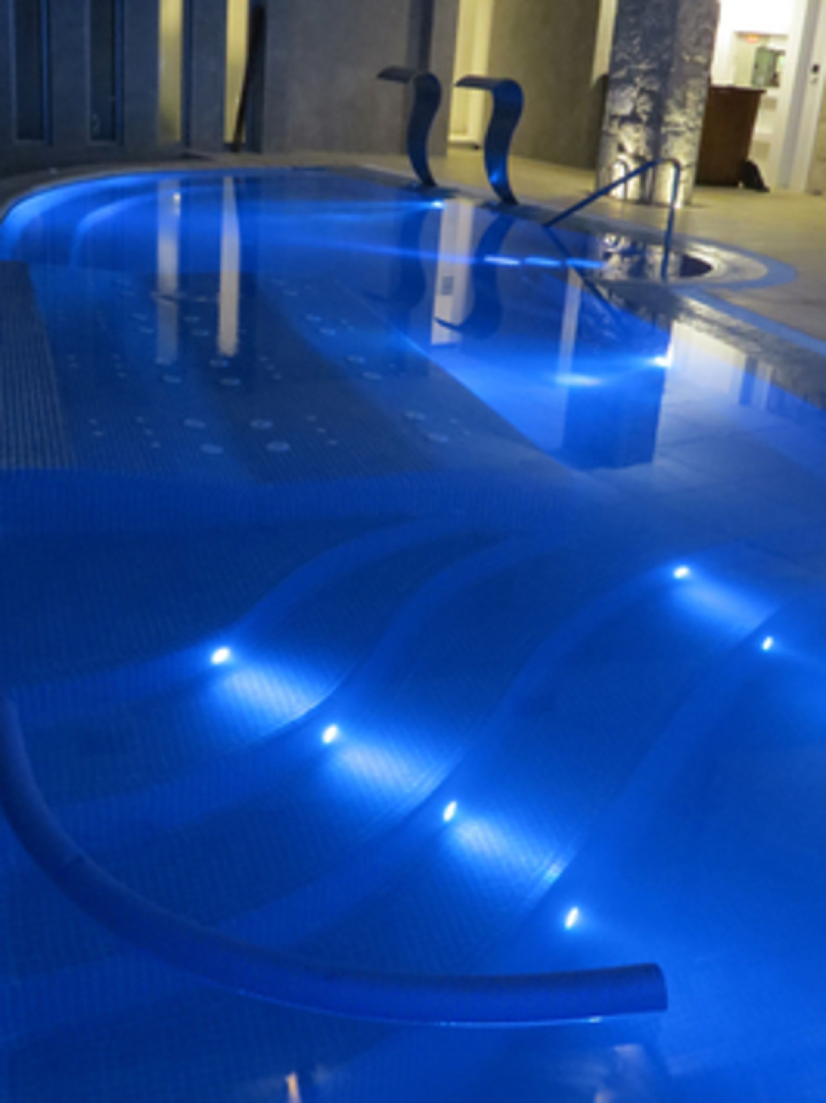 A modern indoor swimming pool with blue lighting.