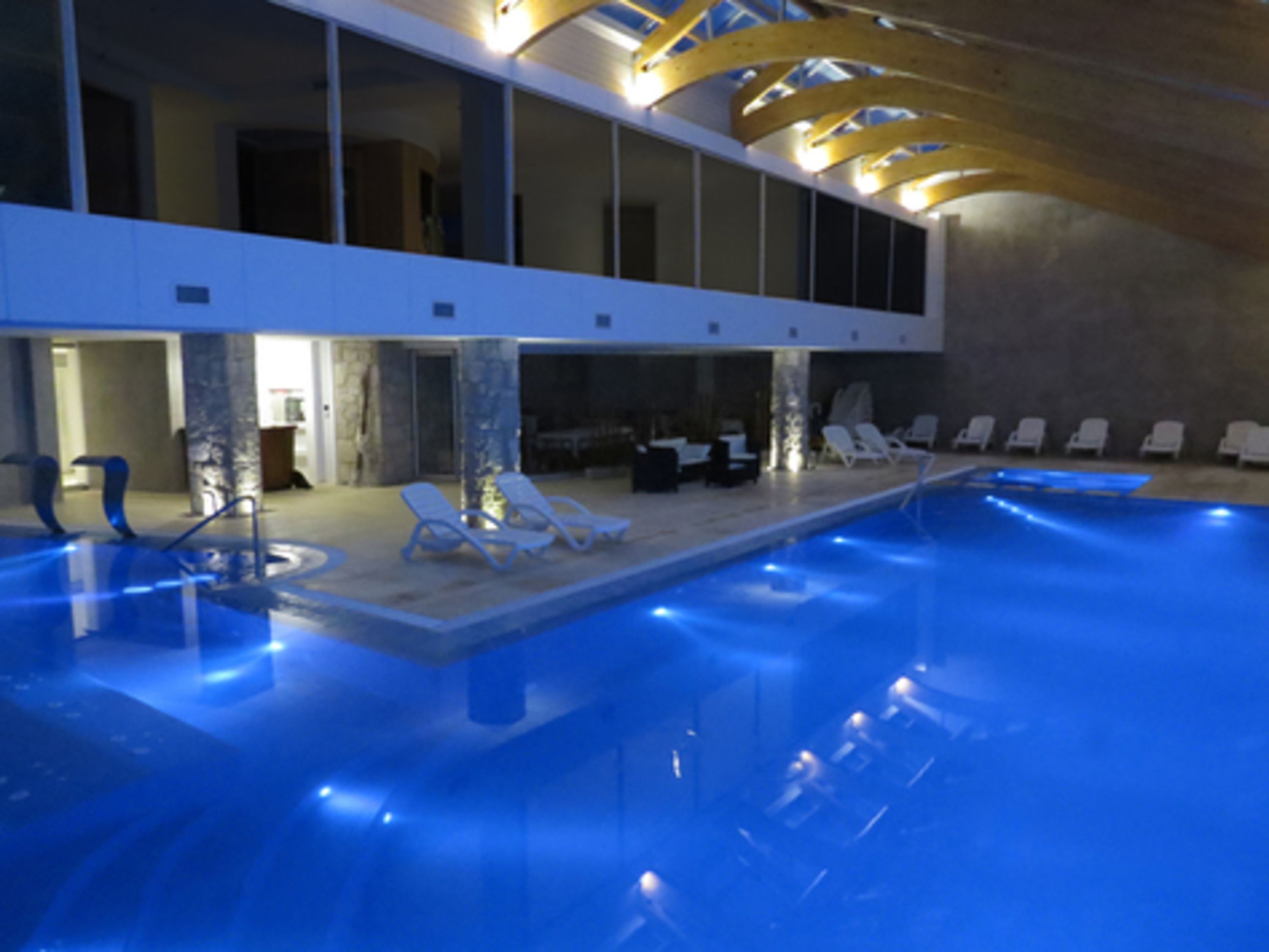 Une piscine intérieure dot ée d’un éclairage bleu, de chaises longues et d’une architecture moderne.