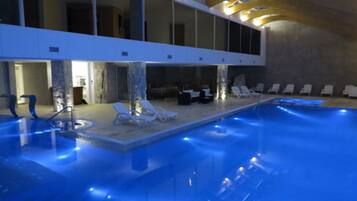 An indoor swimming pool with blue lighting, lounge chairs, and a modern architectural design.