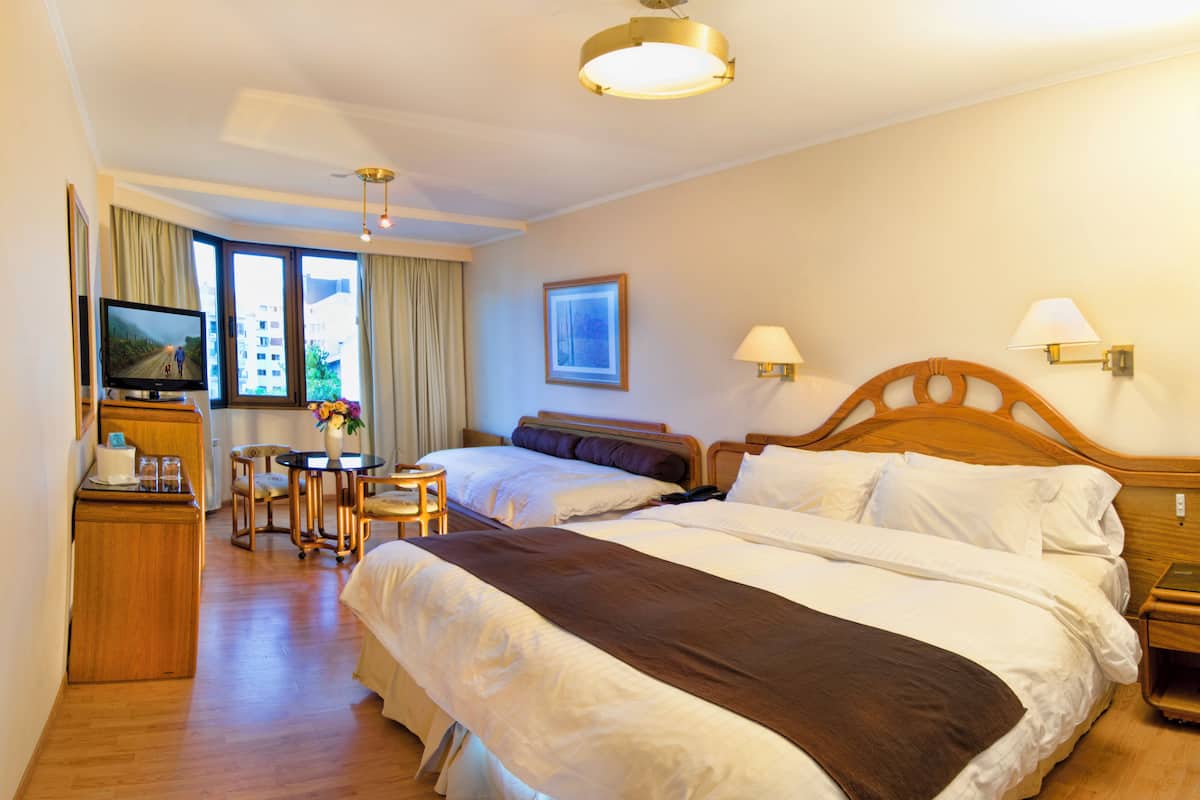 A hotel room with two beds, a desk with a chair, a television, and a window with curtains.