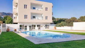 Un edificio moderno de varios pisos con piscina, mobiliario exterior y vistas a la montaña.