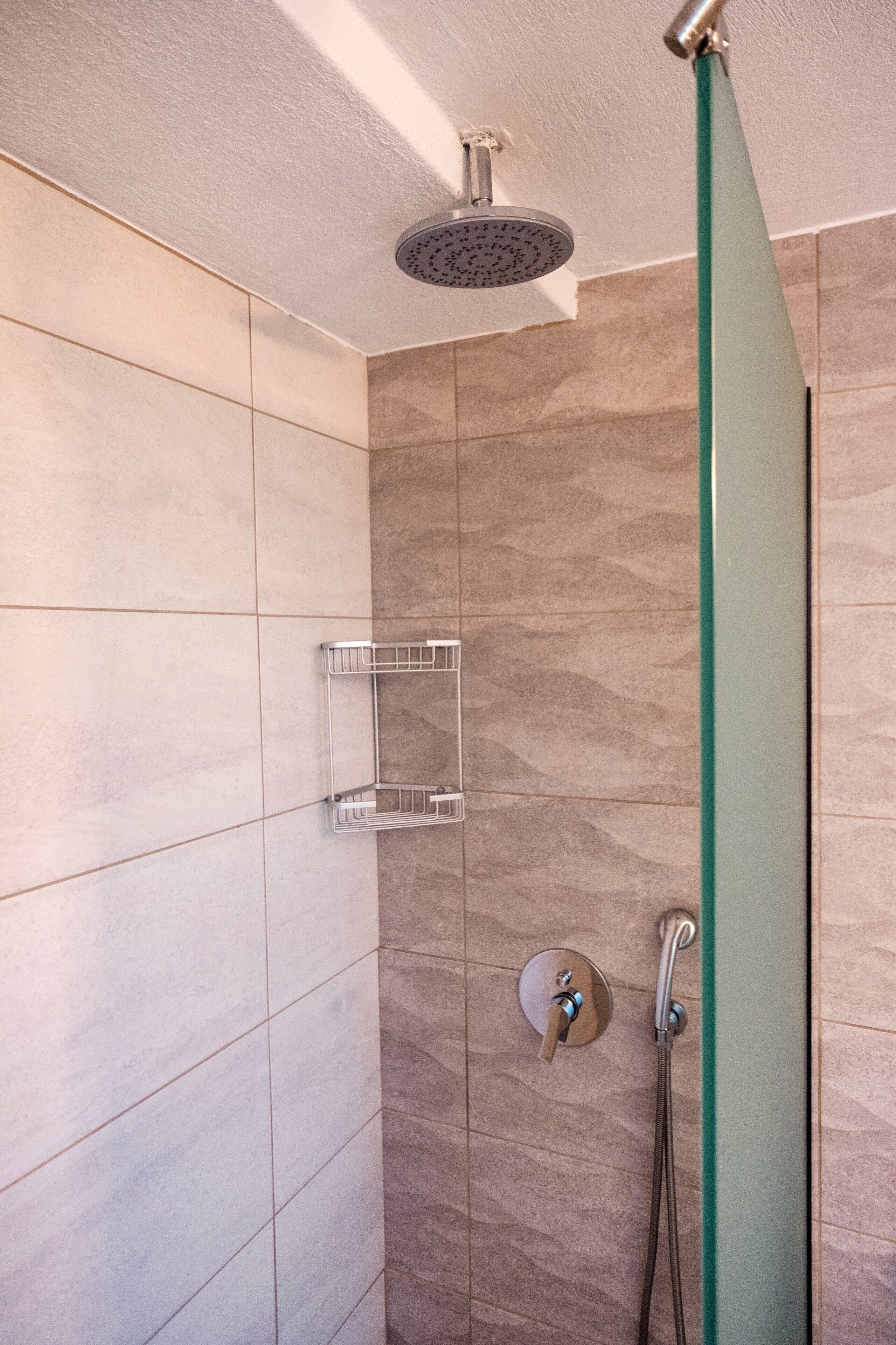 A modern shower with a glass door, a handheld showerhead, and a wall-mounted shelf.