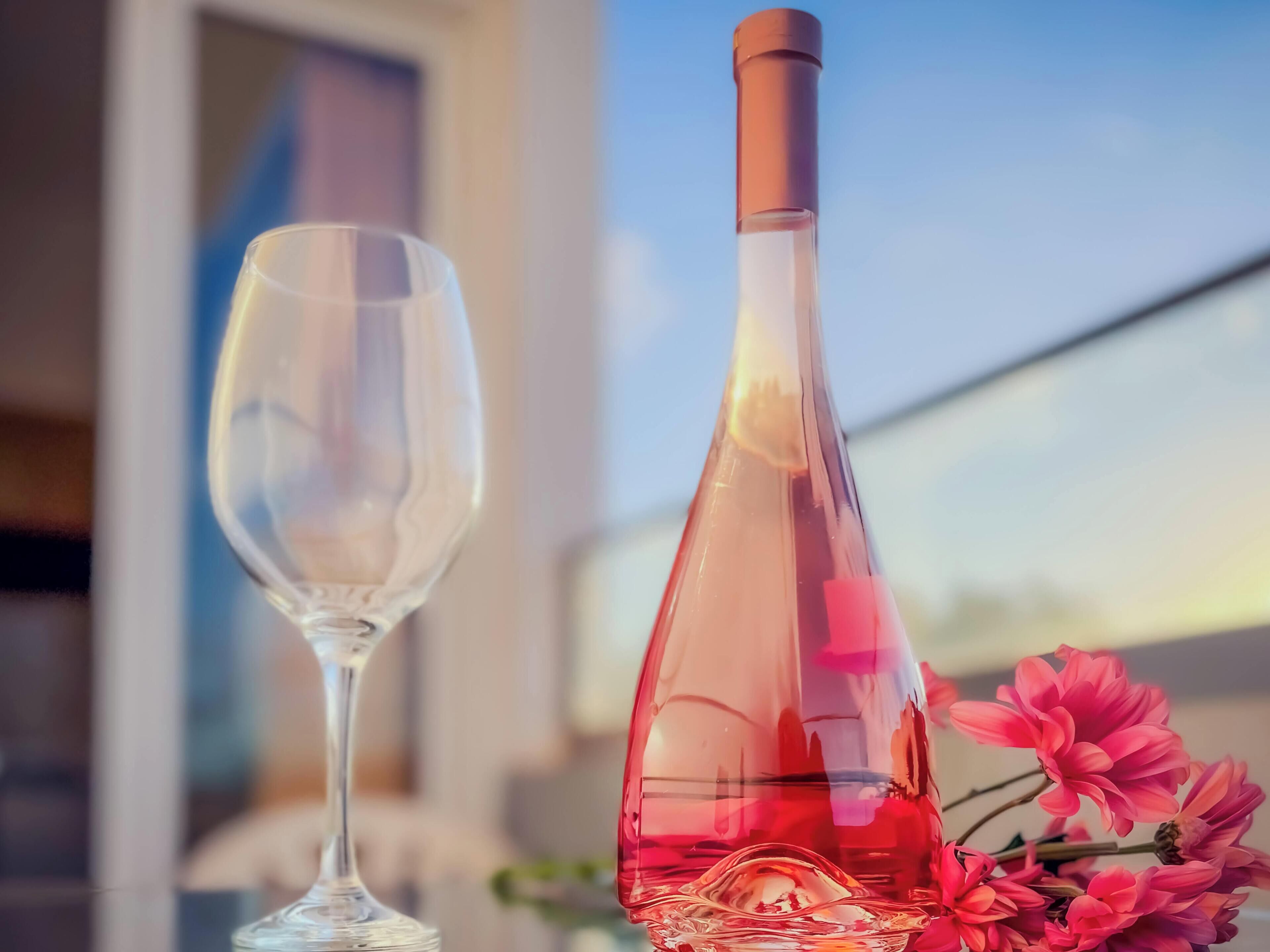 Una botella de vino y una copa sobre una mesa con flores rosadas.