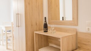 Escritorio de madera con una botella y un vaso, un espejo y un armario en una habitación de hotel.