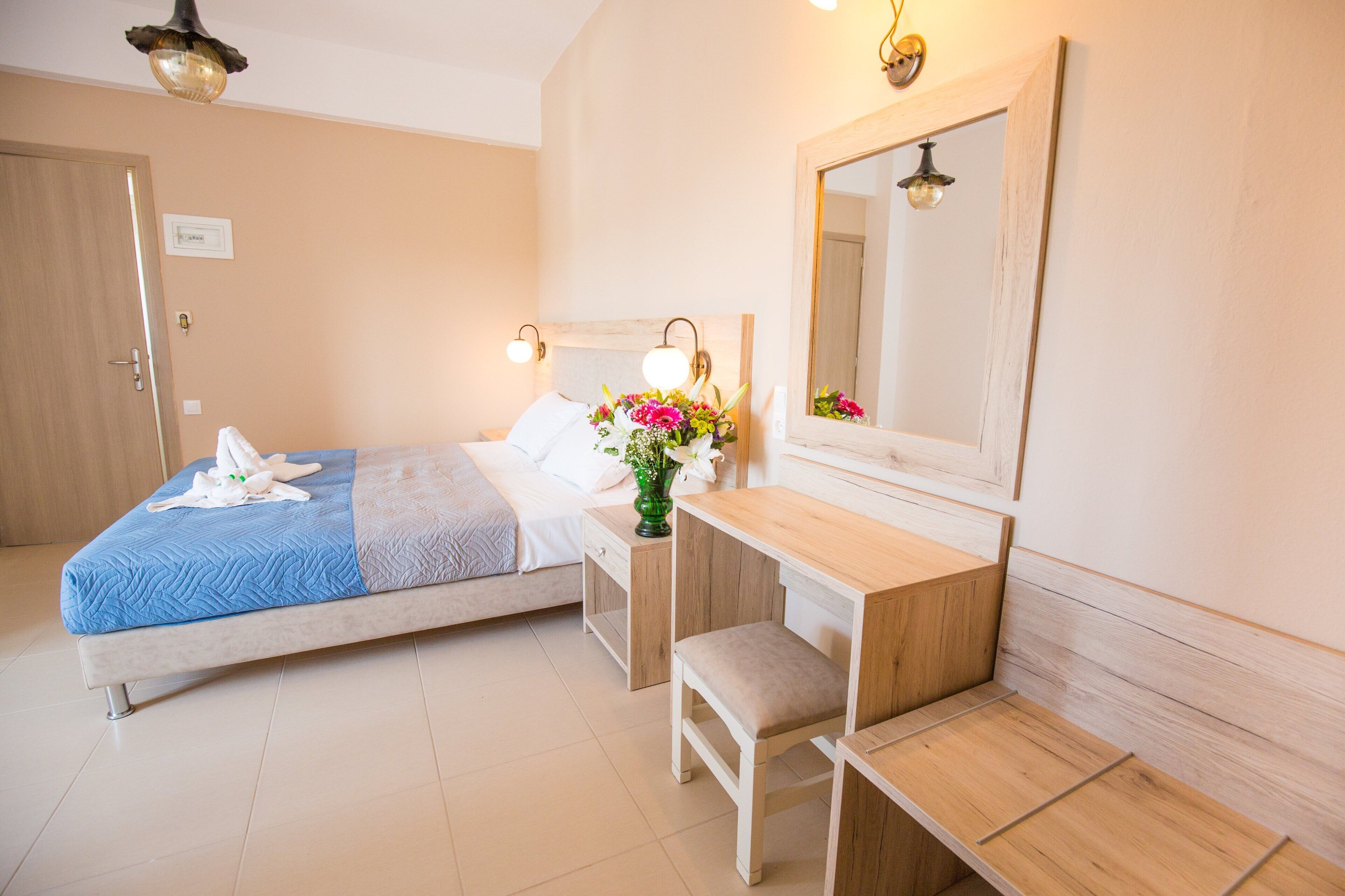 Ein Hotelzimmer mit einem Bett, einem Holztisch, einem Stuhl, einem Spiegel und einer Vase mit Blumen.