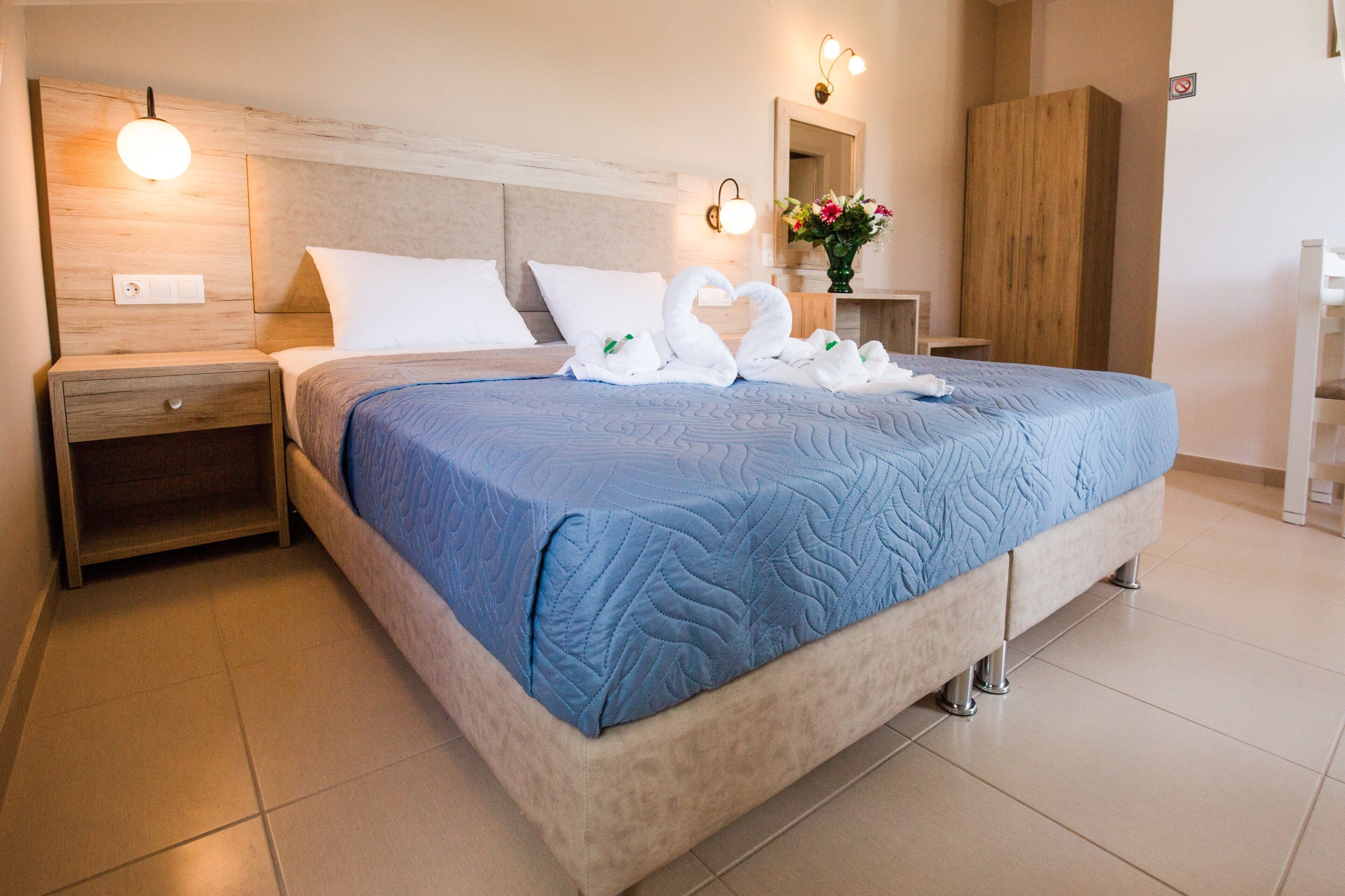 A neatly made bed with a blue quilt, a nightstand with a lamp, and a wooden wardrobe.