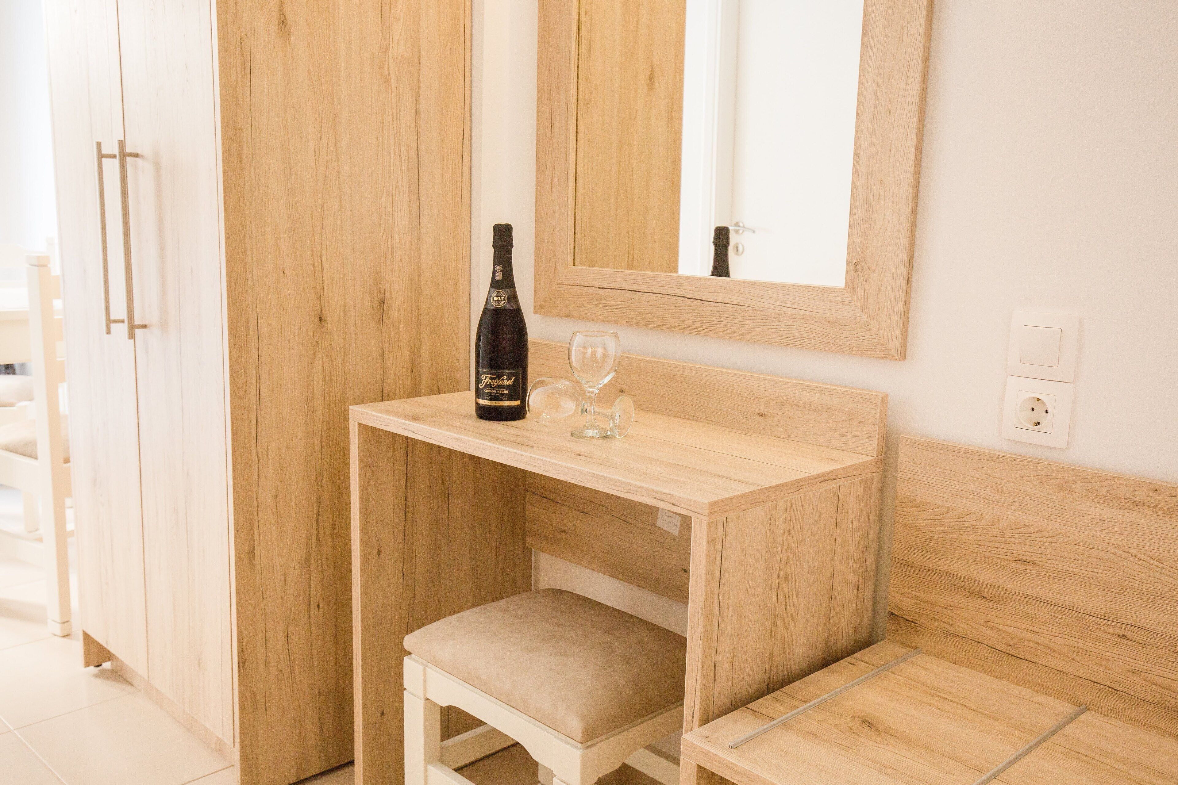 A wooden vanity with a bottle and glass, a mirror, and a small stool.