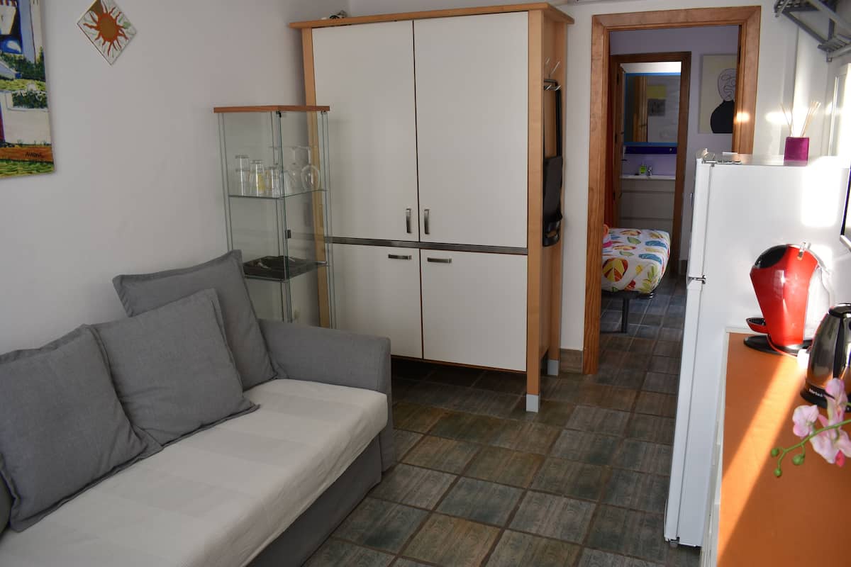 A compact living space with a sofa, a cabinet, a refrigerator, and a small kitchen area.