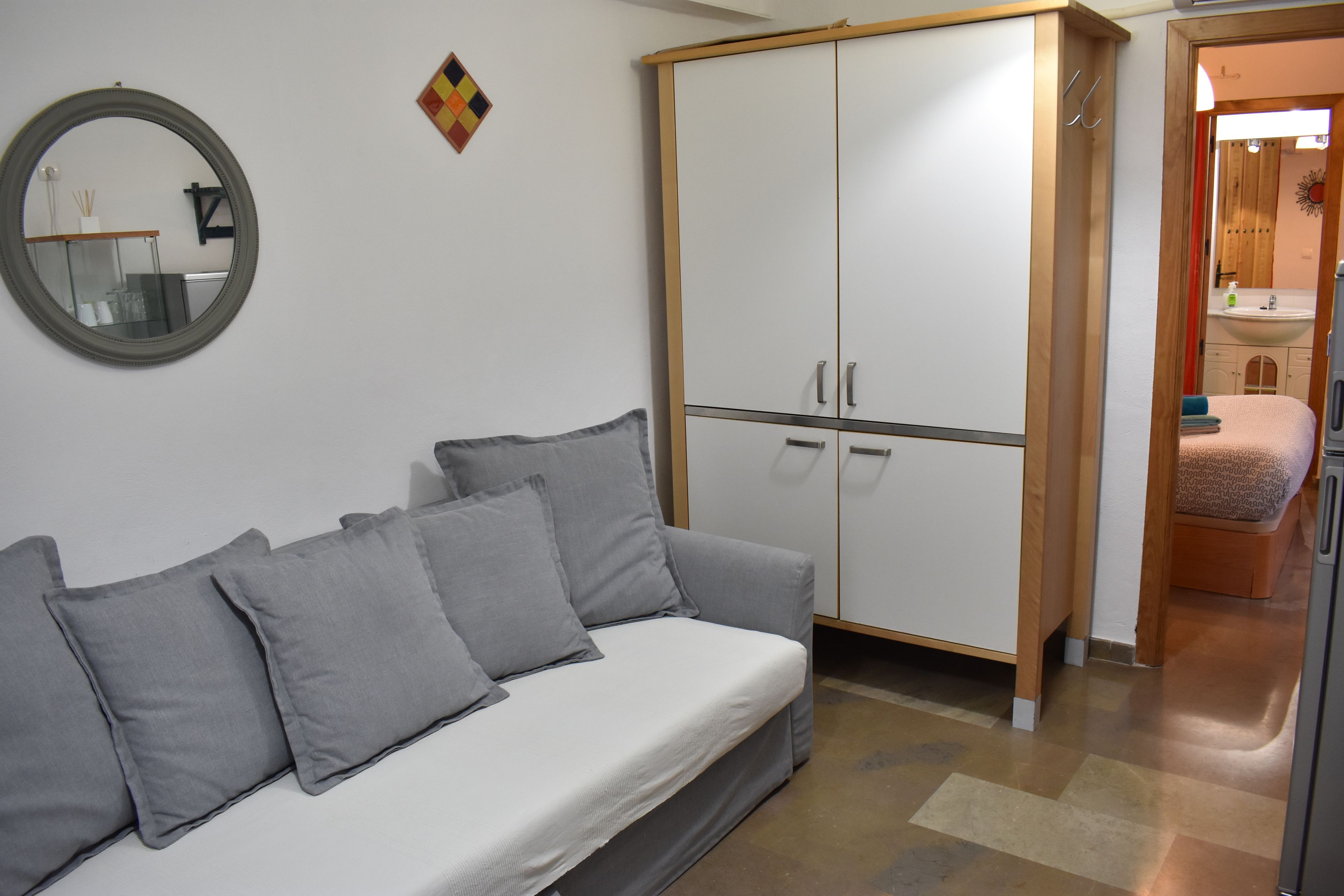 Une pièce avec un canapé gris, une armoire, un miroir et un petit tapis.