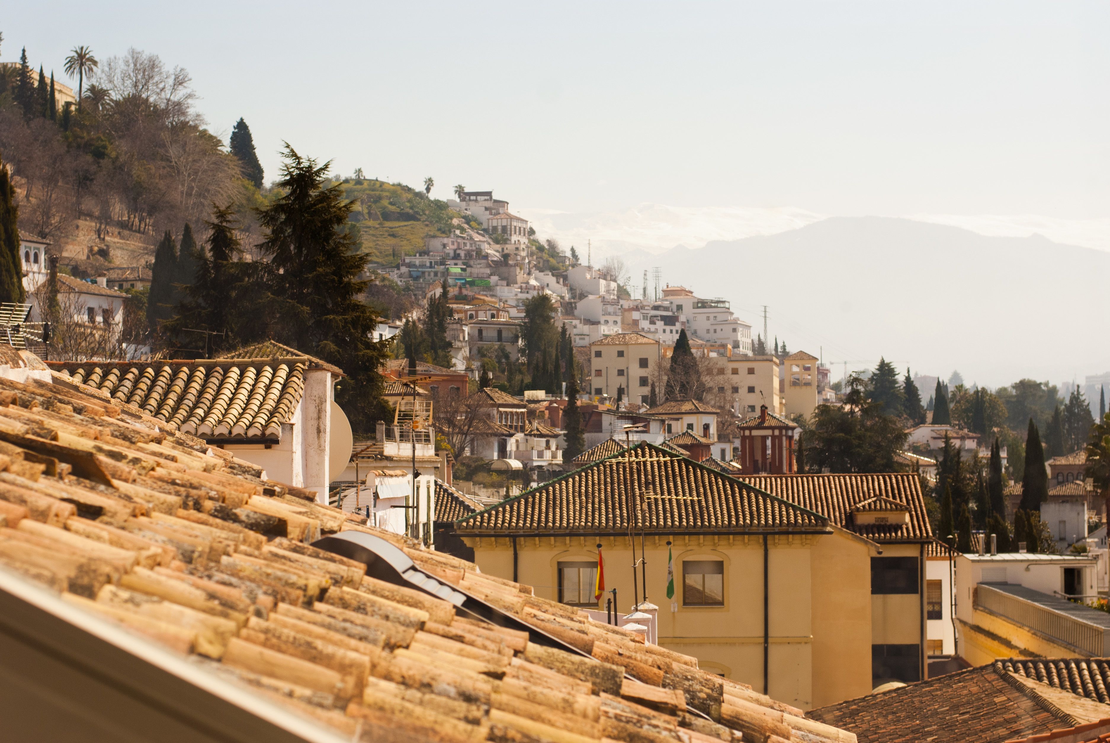 Un pueblo en la ladera con edificios de tejas de color terracota, un edificio amarillo destacado al frente y una montaña en el fondo.