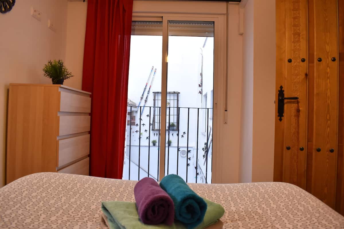 A bedroom with a bed, a wooden wardrobe, a red curtain, and a balcony with a railing.