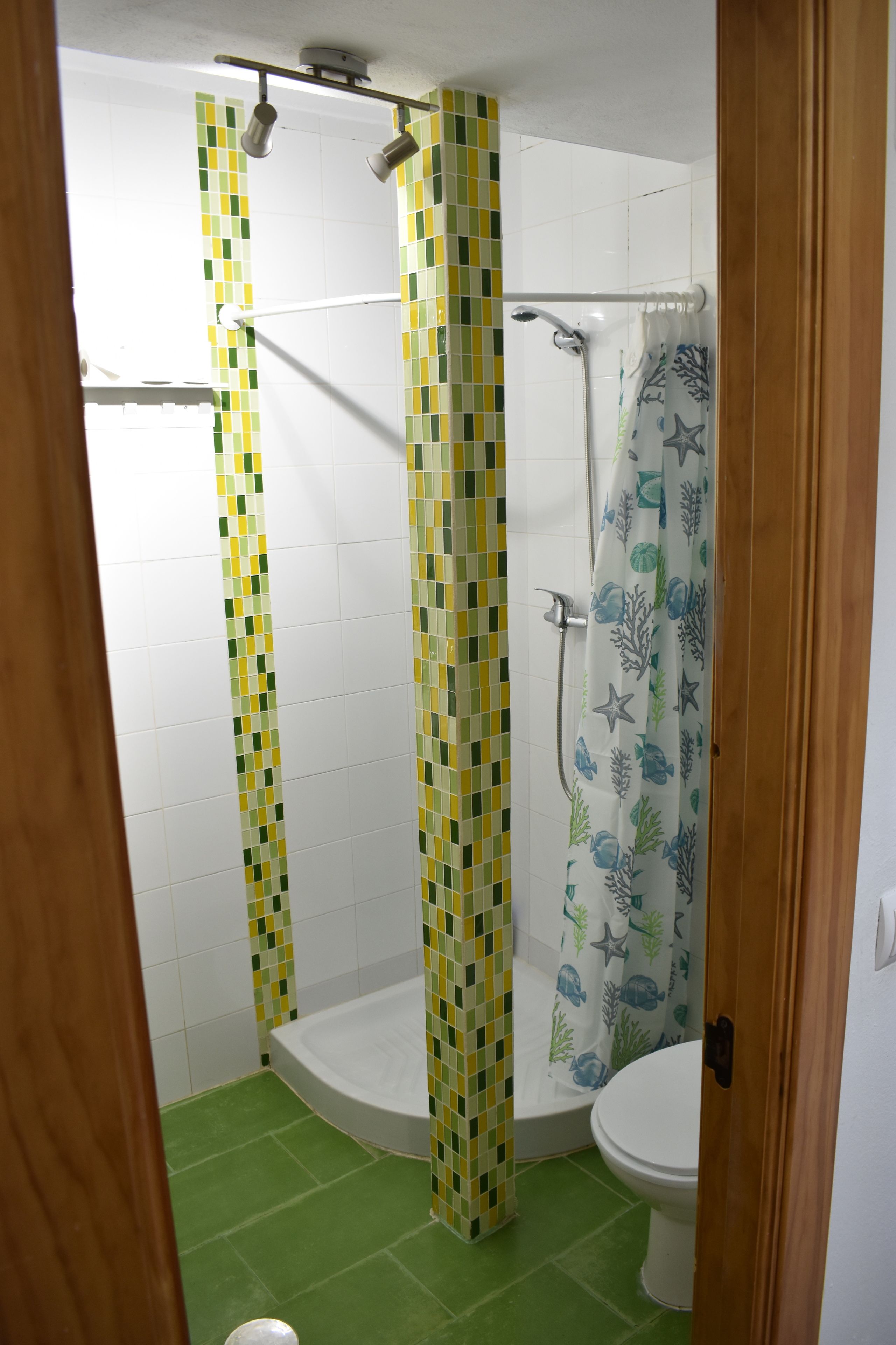 A bathroom with a shower, toilet, and green floor tiles.