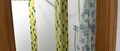 A bathroom with a shower, toilet, and green floor tiles.
