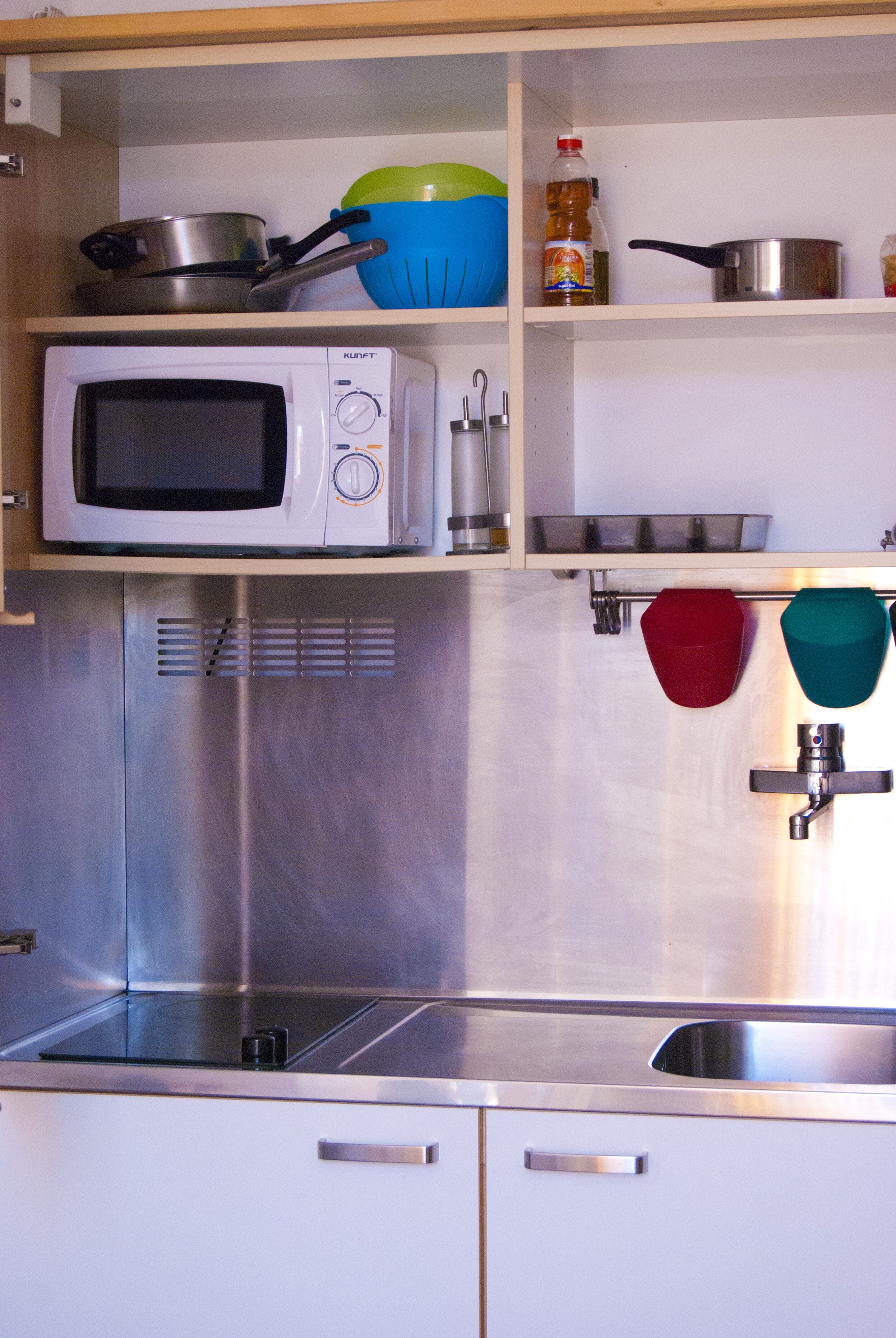 Een keuken met een magnetron, roestvrijstalen apparatuur en planken met pannen en kommen.
