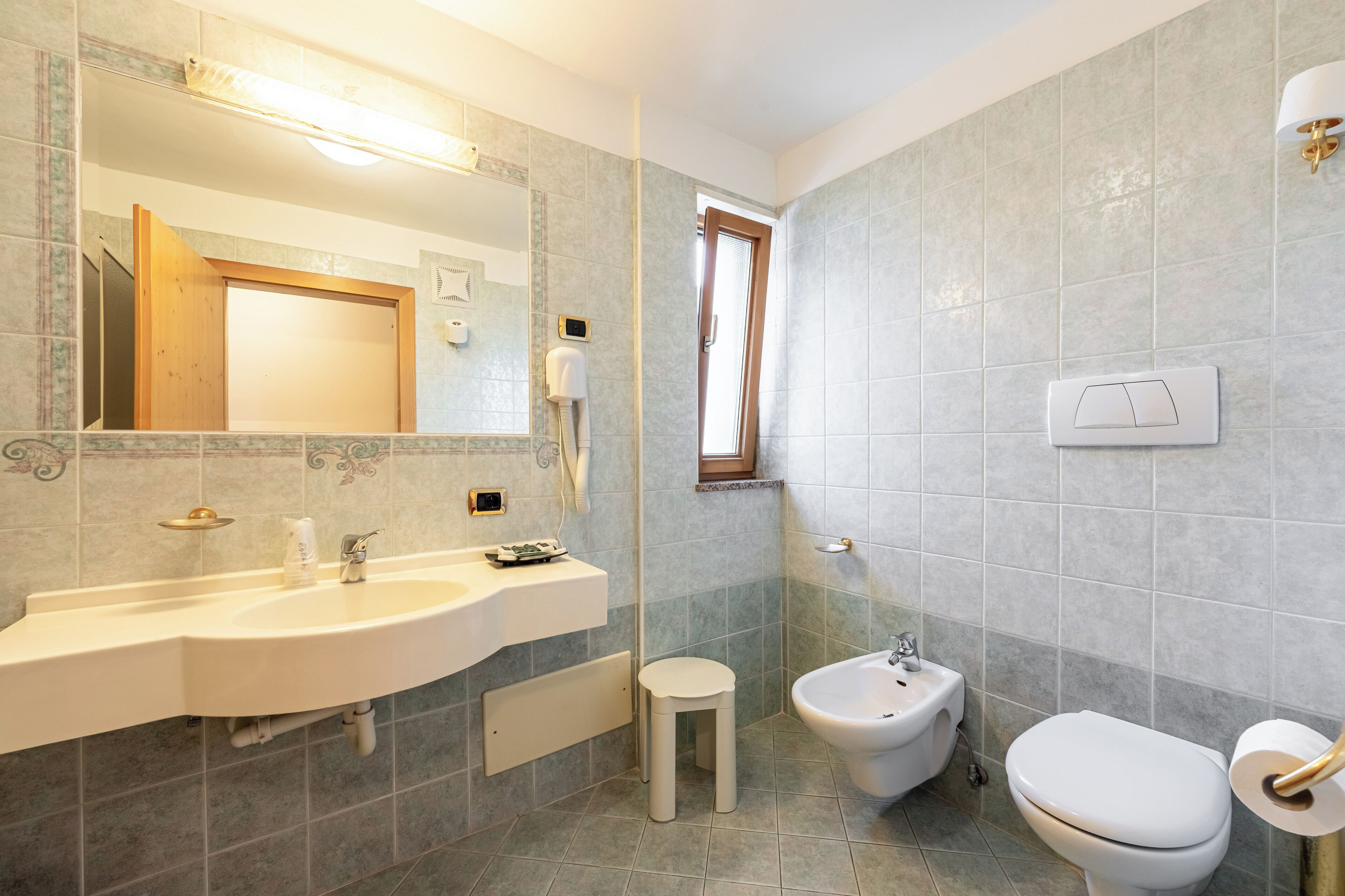 Un bany amb un lavabo doble, un tamboret petit, un vàter i un lavabo.