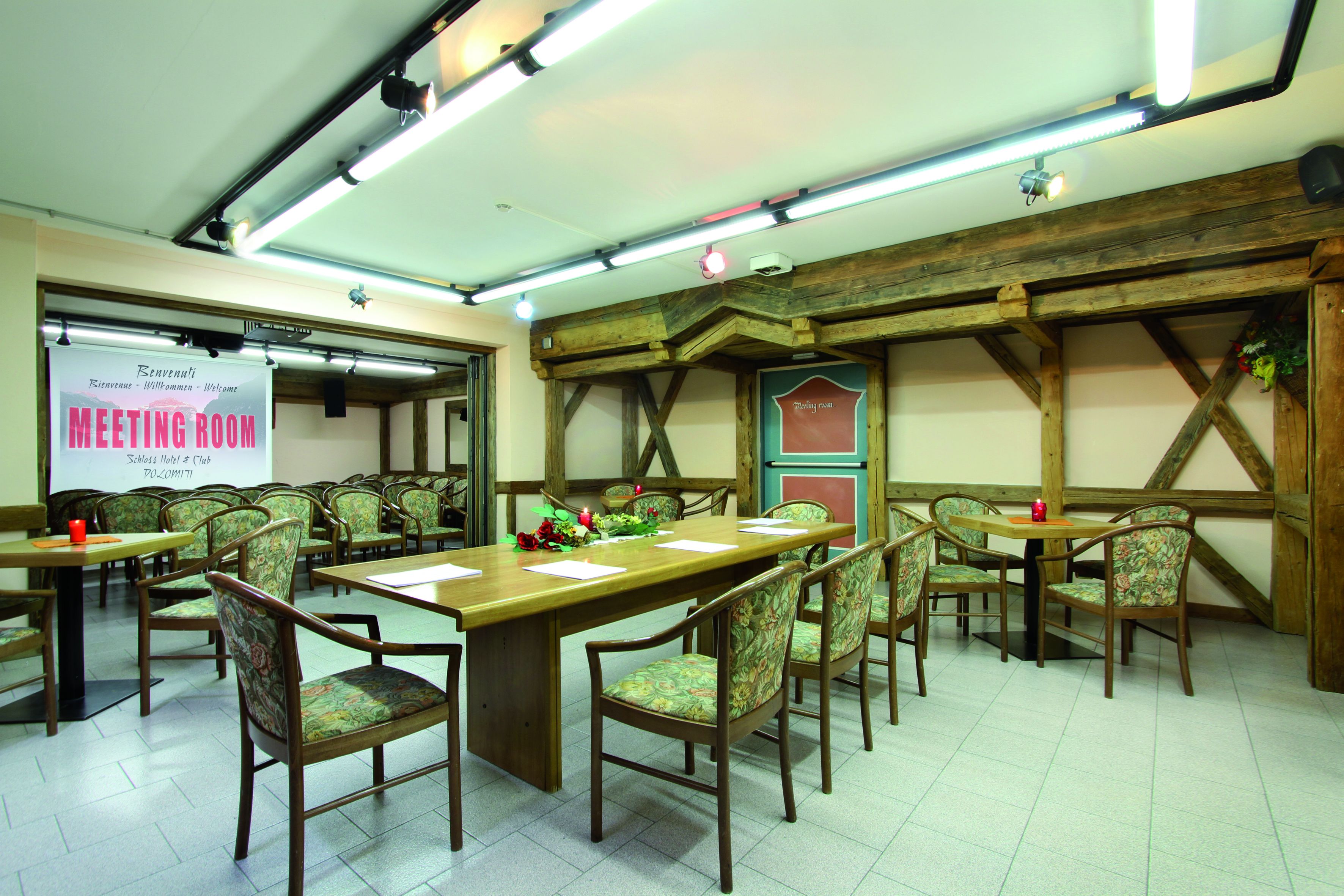 Une salle de réunion avec des tables et des chaises en bois, un écran de projection et un panneau indiquant qu’il s’agit d’une salle de réunion.