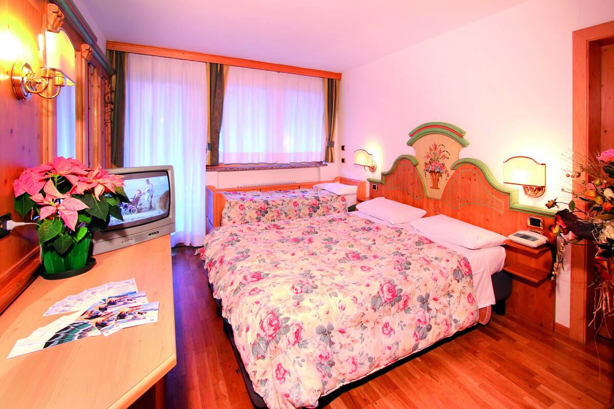A hotel room with two beds, a TV, a desk with papers, and a plant.