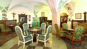 Une pièce dotée d’un plafond voûté, de chaises à motifs verts disposées autour d’une table centrale et d’une cheminée dont le foyer est orné de carreaux verts.