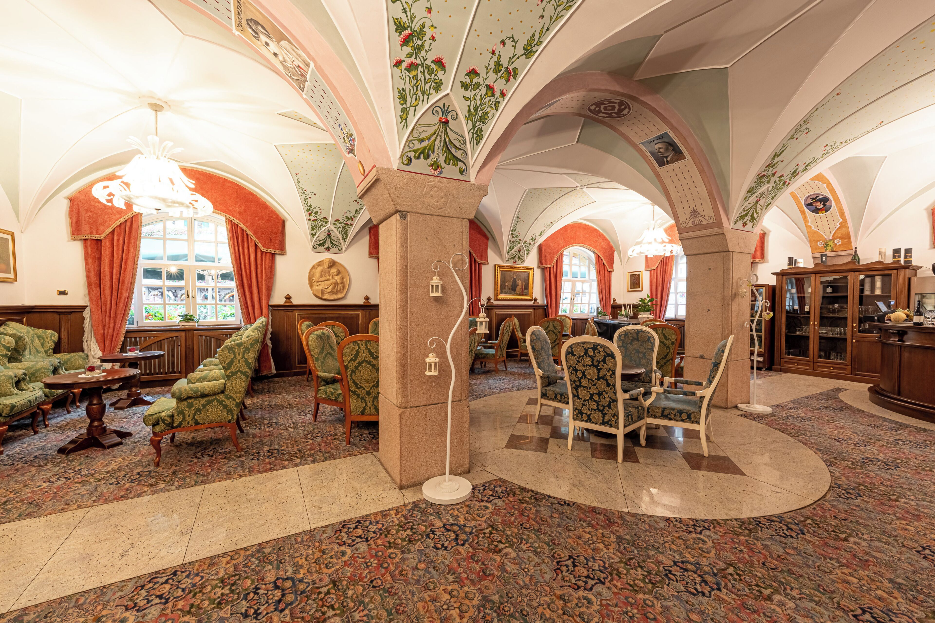 Un'ampia hall con soffitti a volta alti, decorazioni floreali elaborate e diverse disposizioni di posti a sedere, tra cui divani e poltrone.