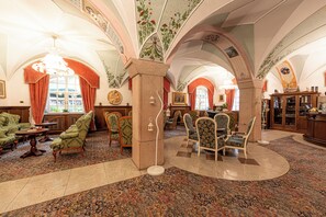 A spacious lobby with high arched ceilings, ornate floral decorations, and a variety of seating arrangements including sofas and armchairs. - Schloss Hotel Dolomiti  (Canazei)