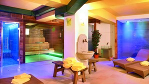 Un espace de détente avec un bassin en pierre, des bancs en bois et des chaises longues, agrémenté d’un mur en pierre et d’une porte en verre donnant accès à un sauna.