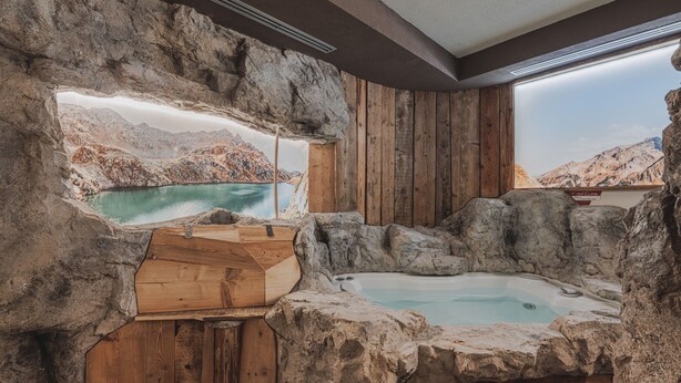 Un bain à remous installé dans un intérieur rustique en pierre, avec des murs en bois et une vue sur un paysage montagneux.