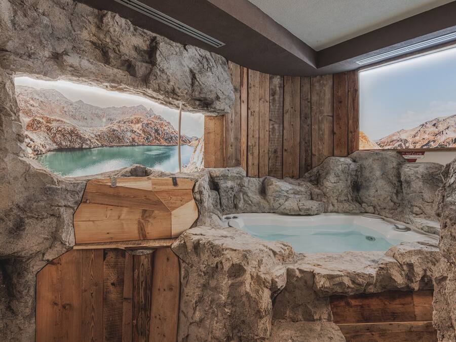 Un jacuzzi en un interior rústico de piedra con paredes de madera y vistas a un paisaje montañoso.