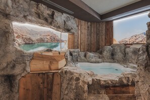 A hot tub set in a rustic stone interior with wooden walls and a view of a mountainous landscape. - Bellavista (Cavalese)