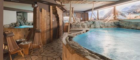 A spa area with a stone floor, wooden seating, and a pool with a mountainous view.