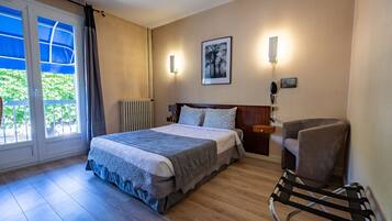 Quarto de hotel com uma cama, uma cadeira, um radiador e uma janela com cortinas.