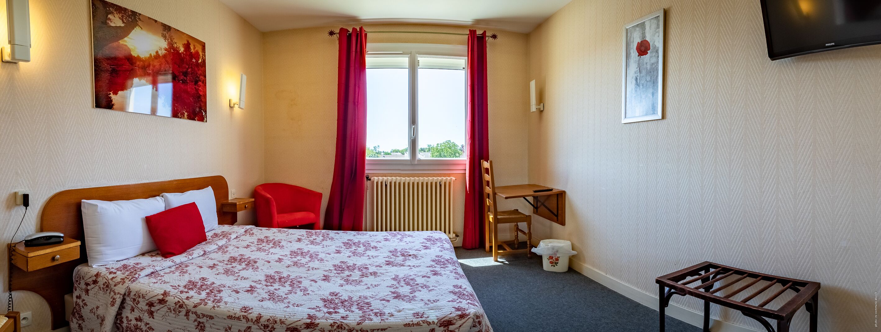 A hotel room with a bed, a chair, a desk, a radiator, and a television.